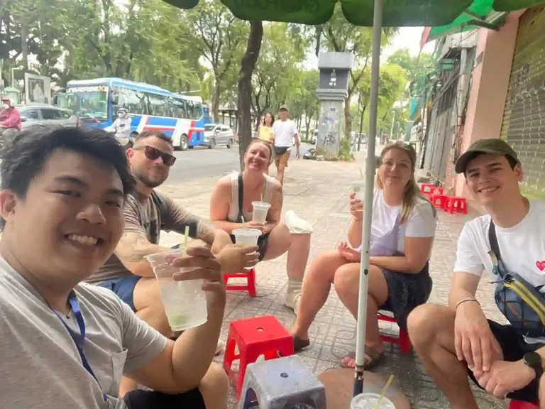 Travelers enjoying local drinks and conversations on a Saigon sidewalk